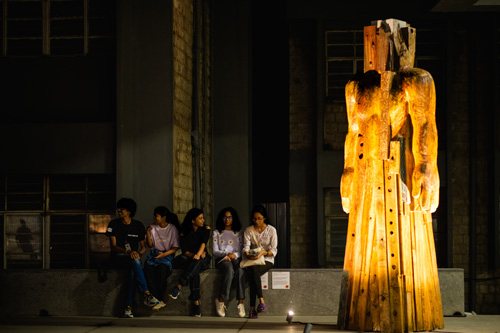 A lit wooden figure in a dark courtyard