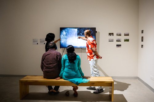 Visitors on a bench watching a screen