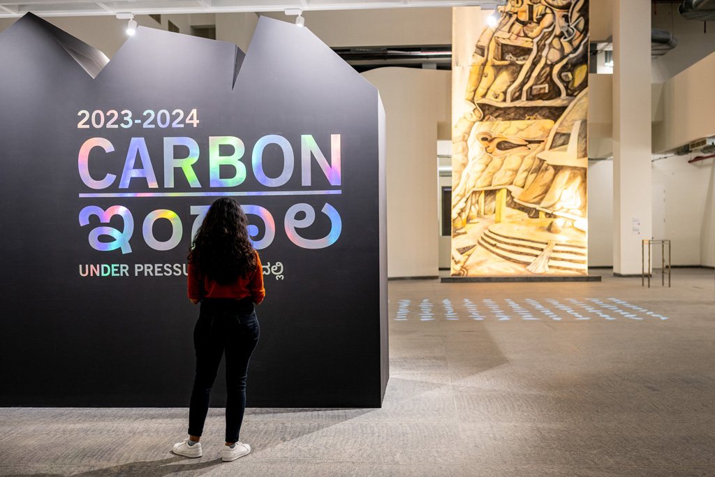 A visitor at the entrance to CARBON beside a tall carved panel